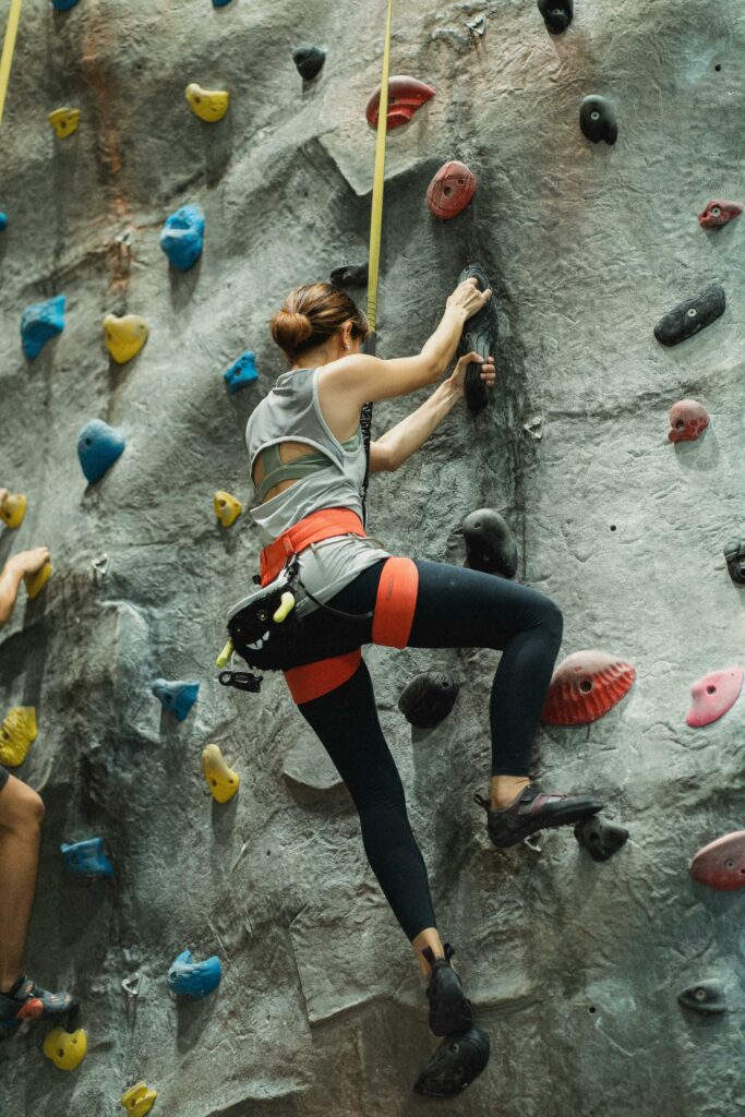 Activités Full body of woman in sportswear training on climbing wall during workout in gym